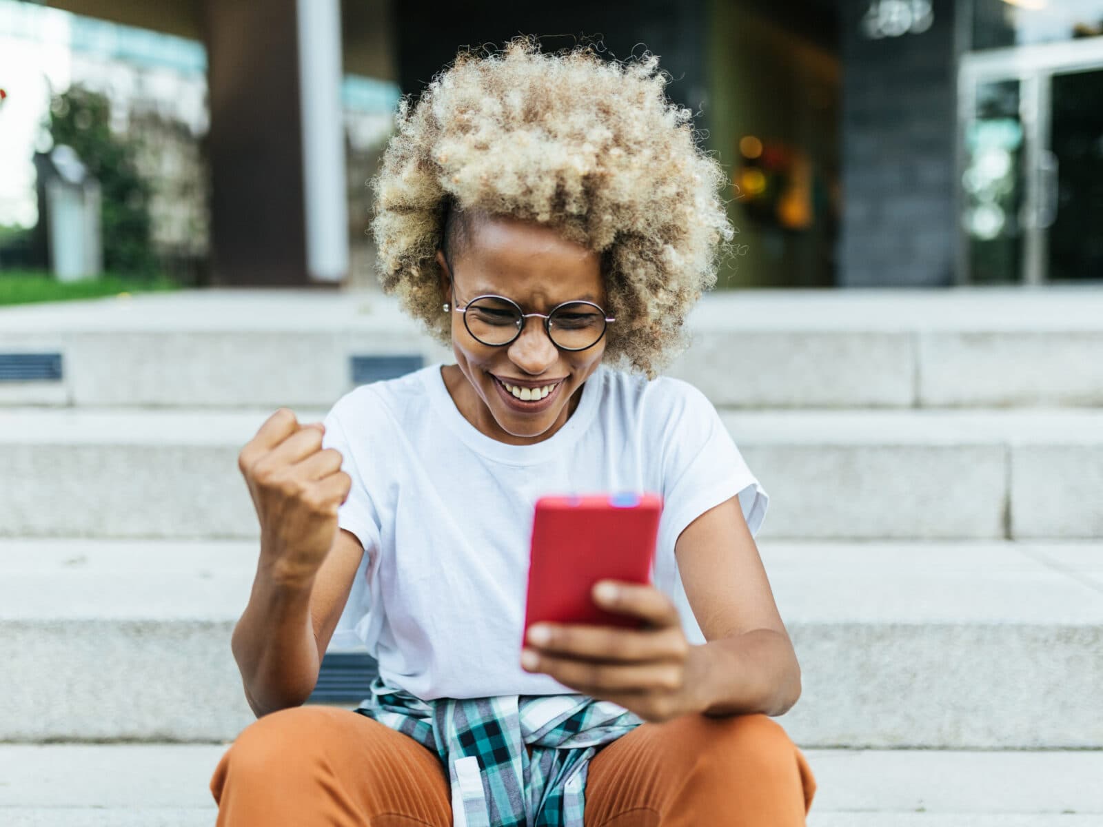 Happy afro woman celebrating victory while receiving good news on her mobile phone. Technology and success concept.