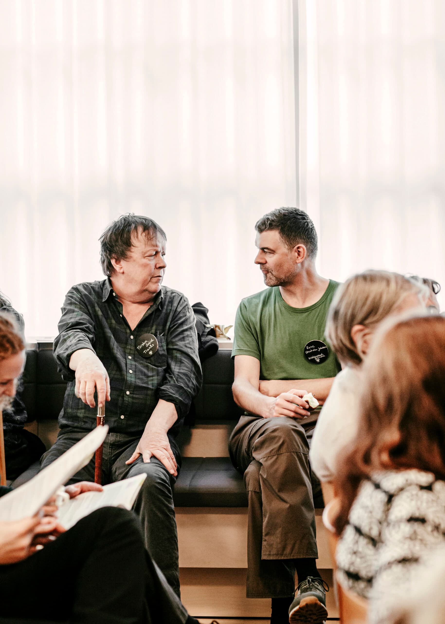 Bilden visar en grupp människor som sitter och verkar vara i en konversation. Två män i förgrunden ...