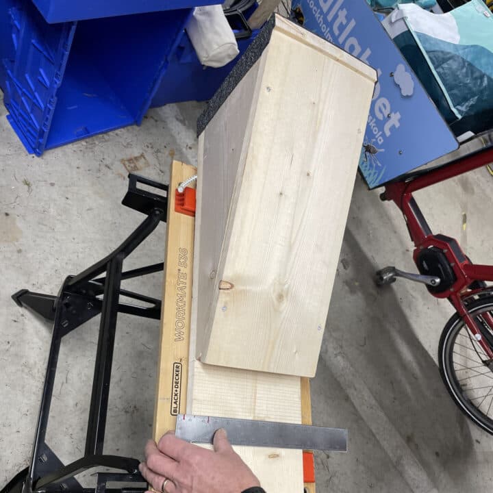 Bilden visar en fladdermusholk, placerad på en arbetsbänk. En person håller en linjal mot träet för ...