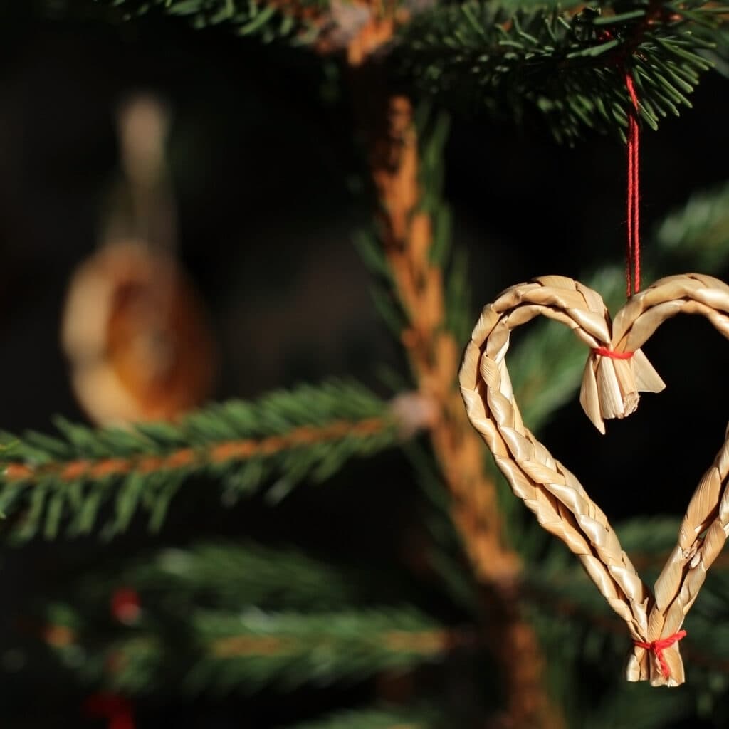 Närbild på hjärtformad halmdekoration som hänger i en julgran