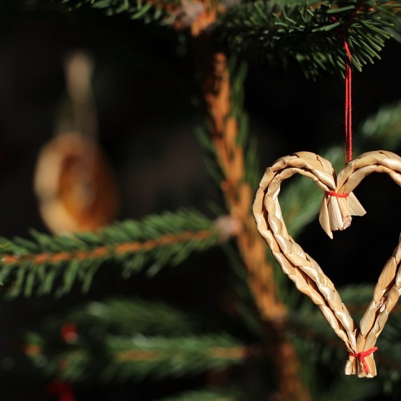 Närbild på hjärtformad halmdekoration som hänger i en julgran