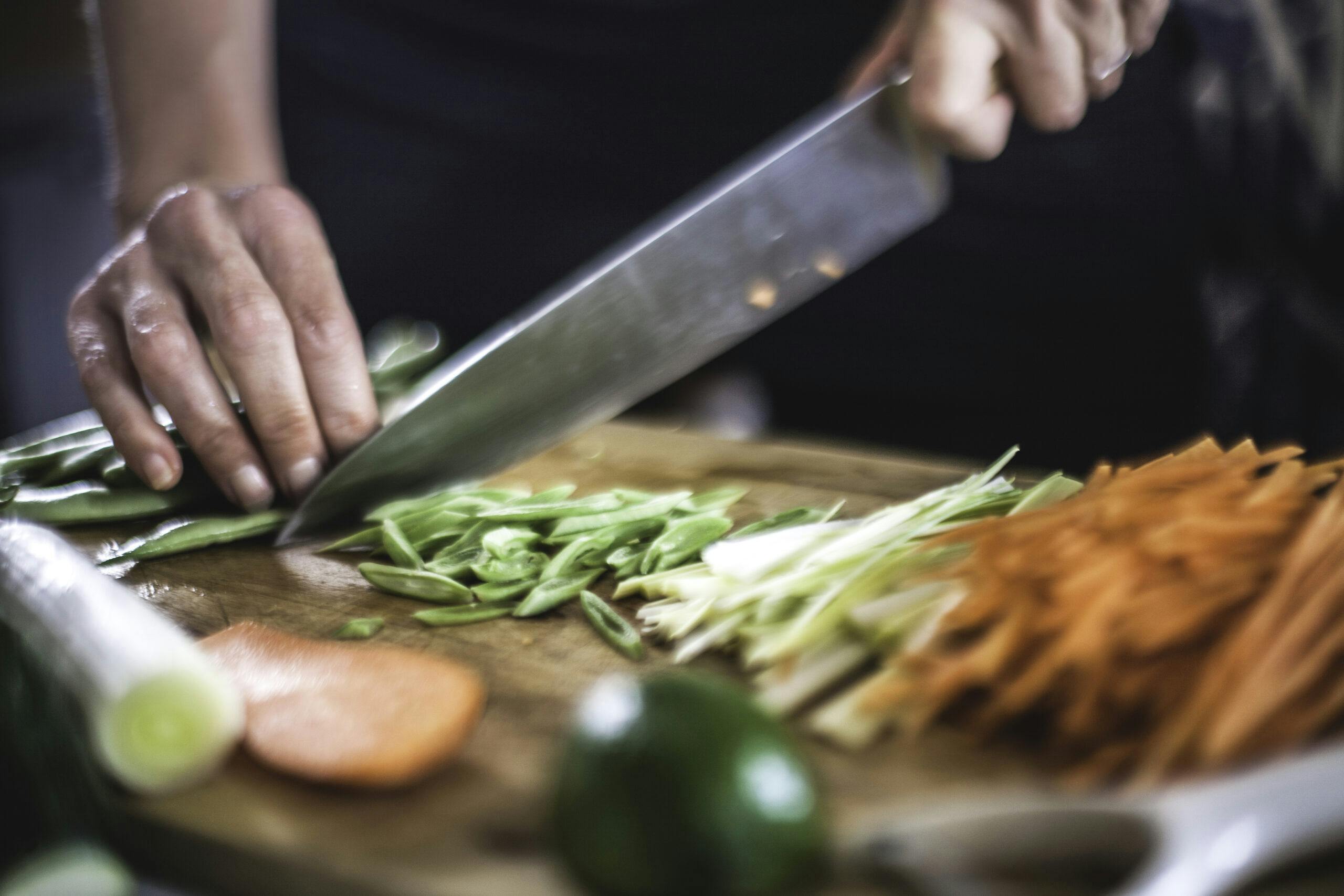 Närbild på en kocks hand som skär grönsaker