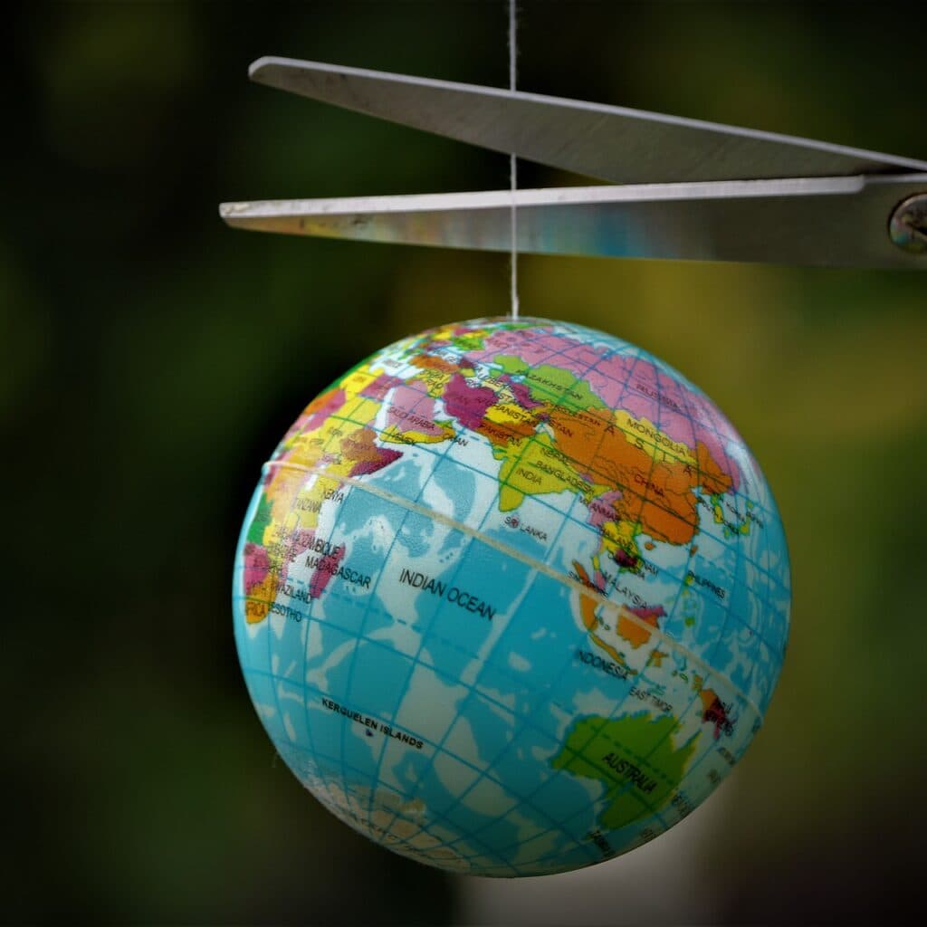 Jordklot som hänger på en skör tråd som klipps av med en sax.