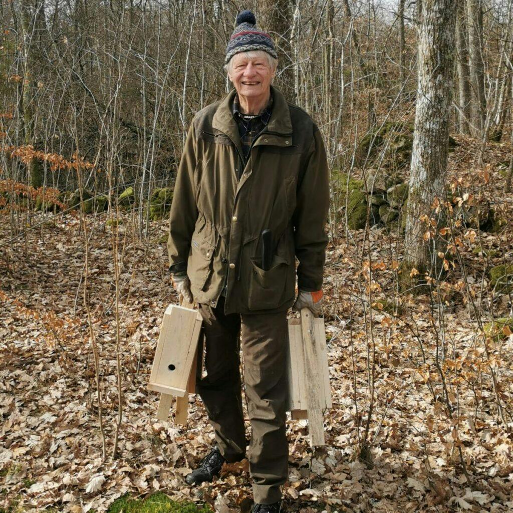Ingvar Arvidsson står i skog och håller i fågelholkar. Bilden har använts för personporträtt av Ingvar på sociala medier.