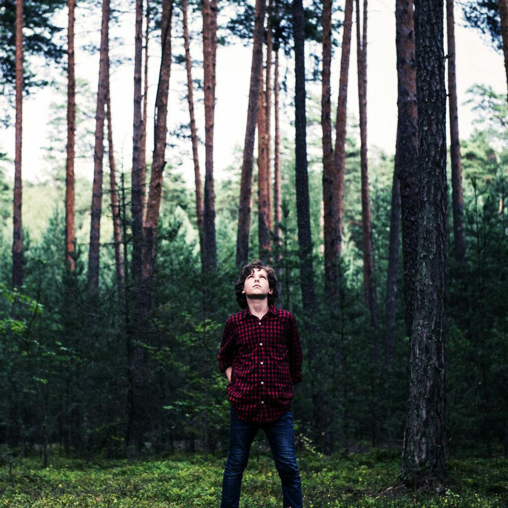 Pojke i rutig skjorta står i en skog och tittar rakt upp i luften.