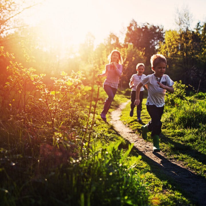 Tre glada barn springer på en stig i solnedgången.