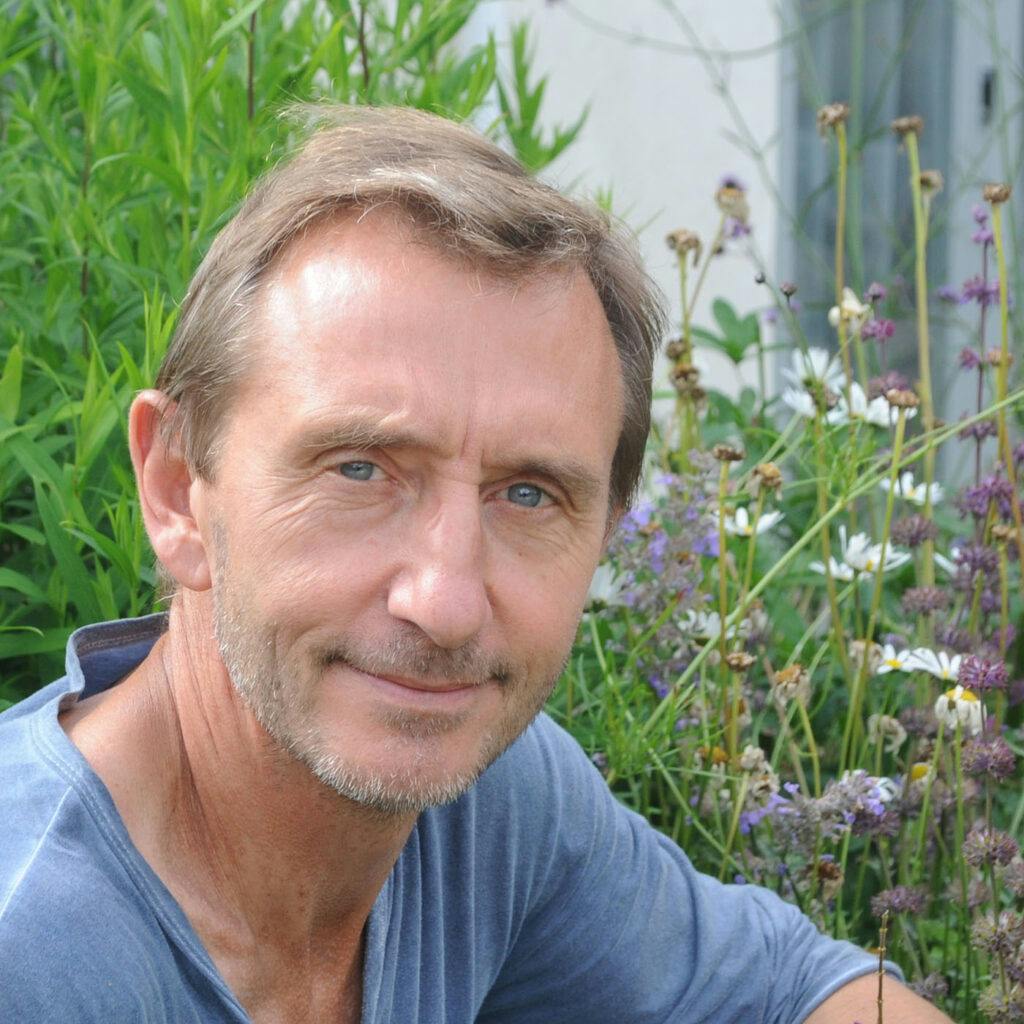 Dave Goulson sitter i en trädgård full av blommande väster och bin, och ler mot kameran.