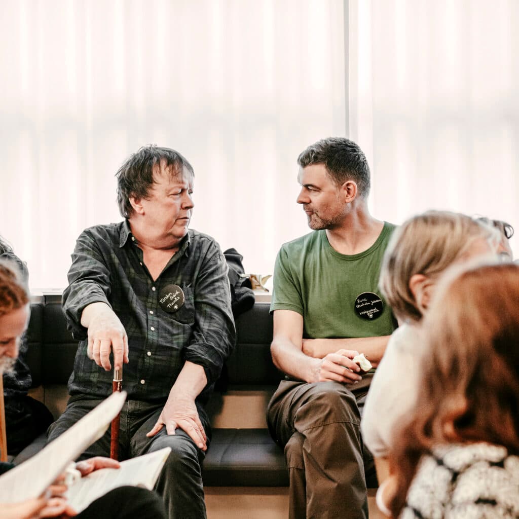 Bilden visar en grupp människor som sitter och verkar vara i en konversation. Två män i förgrunden ...