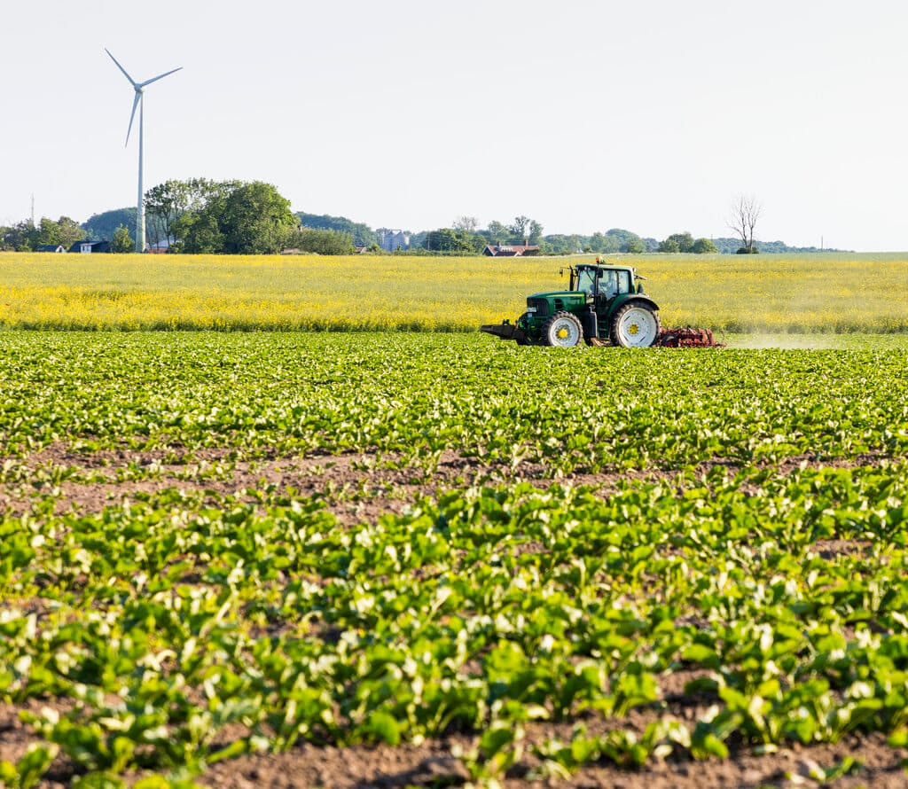 Traktor som kör på fält. Vindkraftverk i bakgrunden.
