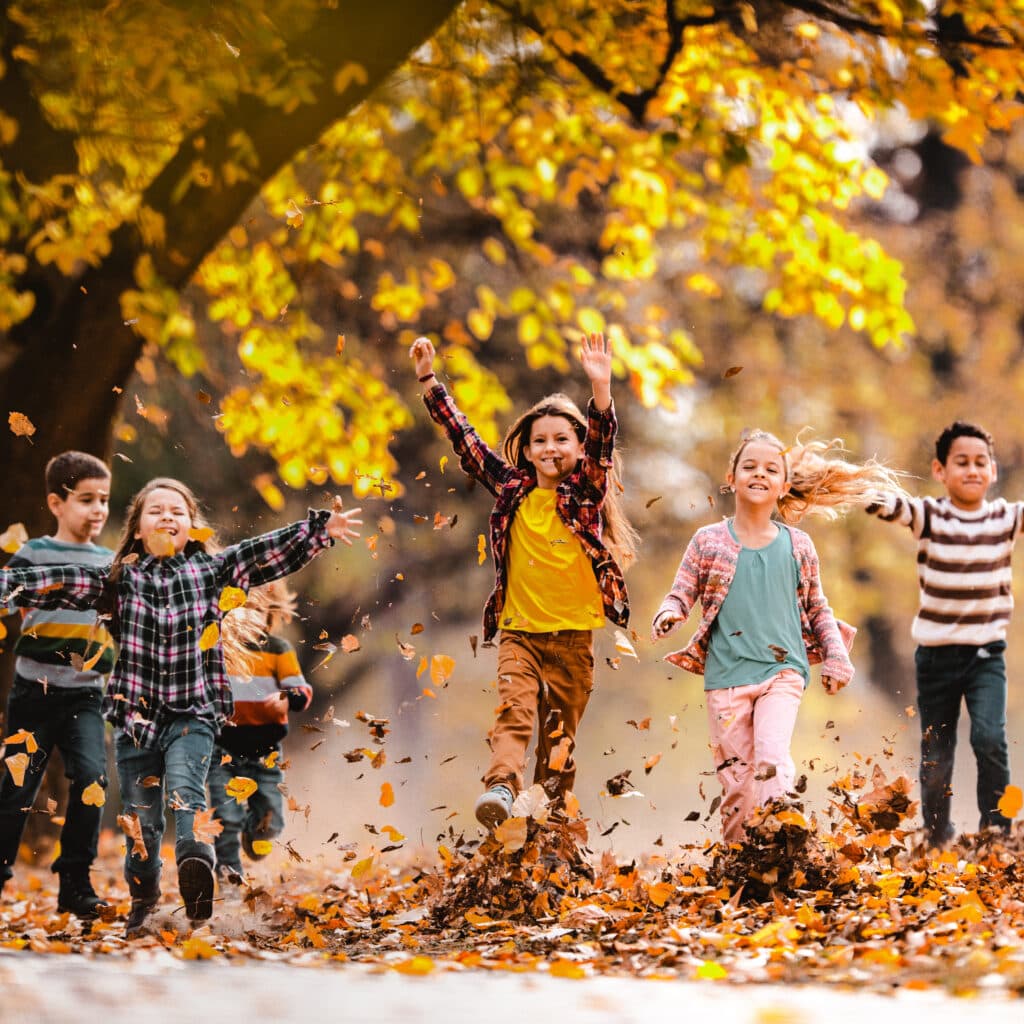 Large group of happy kids having fun while running through autumn leaves in the park.